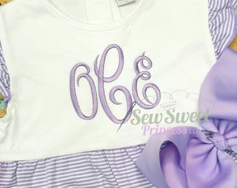 Peut inclure: Robe blanche et lavande à rayures avec un grand monogramme lavande. La robe présente des manches à volants et un nœud lavande assorti. Le texte "Sew Sweet Princess LLC" est visible.