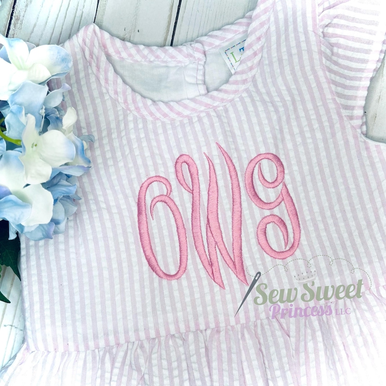 May include: A pink and white striped baby dress with a pink monogram "OWG" embroidered on the front. The dress has a ruffled hem and short sleeves. The text "Sew Sweet Princess LLC" is visible in the bottom right corner.
