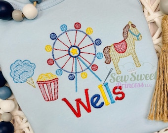 Peut inclure: Body de bébé bleu clair avec un motif de carnaval brodé coloré. Comprend une grande roue, un cheval, de la barbe à papa et du pop-corn. Le nom "Wells" est brodé en rouge, jaune et bleu.