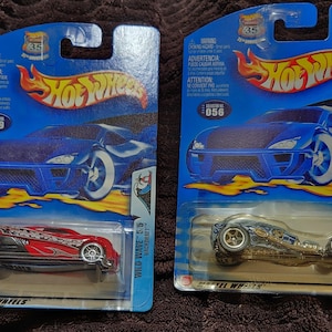 May include: Two Hot Wheels die-cast toy cars in their original packaging. The car on the left is red with black flames and is called "Wild Wave 5/5 Backdraft". The car on the right is silver with blue accents and is called "Sure Crate 2/5".