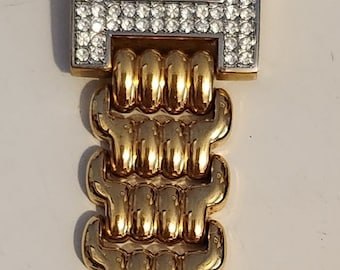Può includere: Un orologio color oro con un quadrante quadrato e una lunetta tempestata di cristalli. Il quadrante dell'orologio è bianco con lancette nere e una scritta nera "QUARTZ". L'orologio ha un cinturino in metallo dorato con chiusura a fibbia.