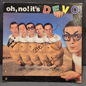 以下が含まれることがあります： 「Oh, No! It's Devo」のアルバムカバー。メンバーがジャガイモの体と白い襟で描かれています。バンド名は上部にカラフルなテキストで表示されています。カバーはバンドメンバーのサイン入りです。