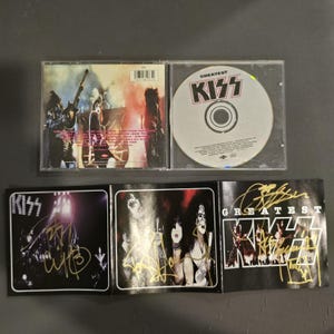 Puede incluir: Un álbum de CD KISS Greatest Hits, abierto para mostrar el CD y el folleto interior. La caja del CD es transparente y el CD tiene el logotipo de la banda. El folleto presenta fotos y firmas de los miembros de la banda.