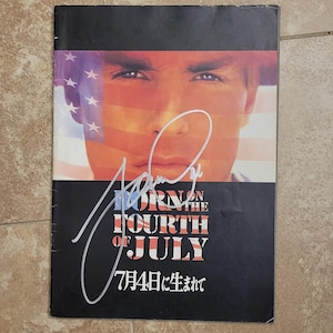 Könnte beinhalten: Ein Filmplakat für "Geboren am 4. Juli" mit dem Gesicht eines Mannes und einem Design der amerikanischen Flagge. Der Titel ist in Rot und Weiß gehalten, darunter die japanische Übersetzung. Enthält eine Unterschrift.
