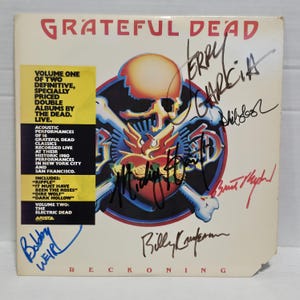 May include: A Grateful Dead Reckoning vinyl record cover featuring a central skull and heart graphic, signed by band members. A yellow sticker on the left lists album details, including live performances of Ripple and Dire Wolf.