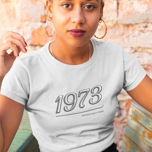 May include: White t-shirt with a silver 1973 graphic and the text "Whatever your vibe is vibe it".