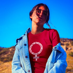 May include: A woman wearing a red t-shirt with a white feminist symbol and the text "Roe. Roe. Roe your boat. Gently down the stream." The woman is wearing a light blue denim jacket.