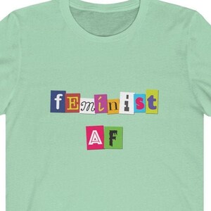 May include: A light green t-shirt with the text "feminist AF" in colorful, cut-out letters.