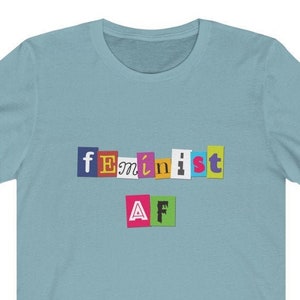 May include: A light blue t-shirt with the text "feminist AF" in colorful, cut-out letters.