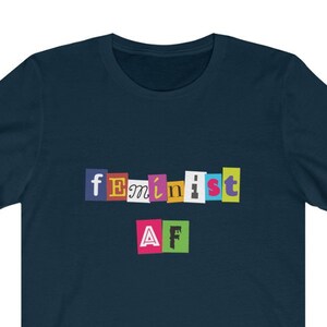 May include: A navy blue t-shirt with the text "feminist AF" in colorful, cut-out letters.
