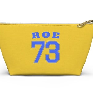 May include: Yellow canvas zippered pouch with a blue and white graphic that says "ROE 73".