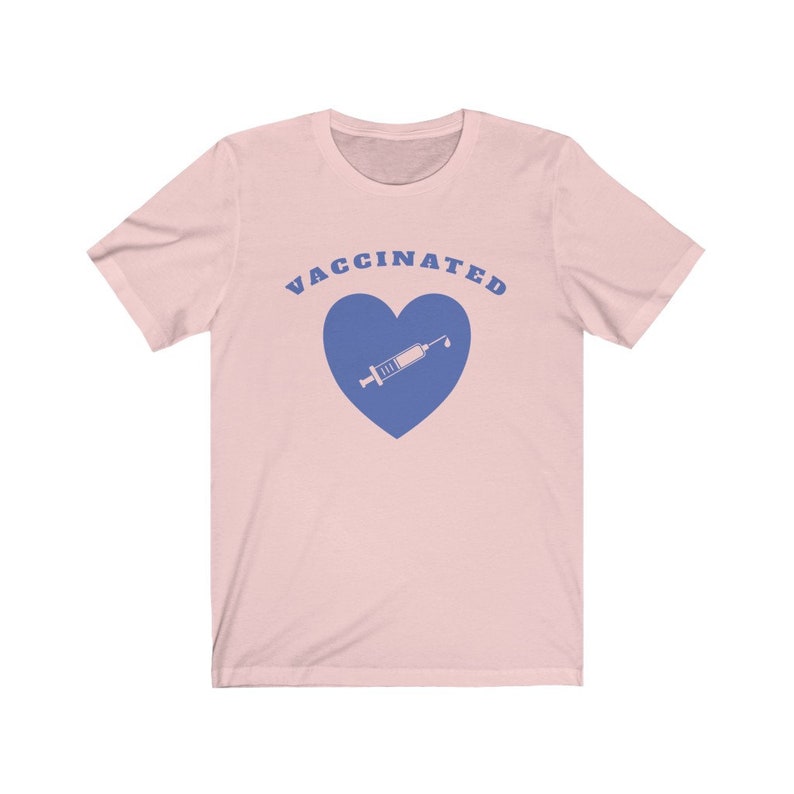 May include: A pink t-shirt with the text "VACCINATED" in blue letters and a blue heart with a syringe inside.