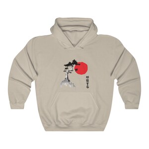 May include: A beige hoodie with a black and white illustration of a pine tree and a red sun. The Japanese text "呼吸する" is printed on the right side of the image.