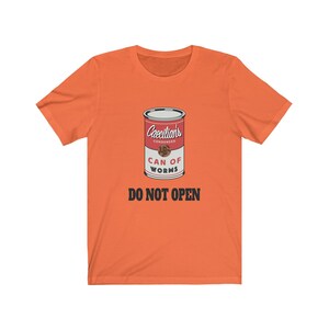 Puede incluir: Camiseta naranja con un gr&aacute;fico de una lata roja etiquetada "Caecilians Condensed Can of Worms" con el texto "Do Not Open" en negro.