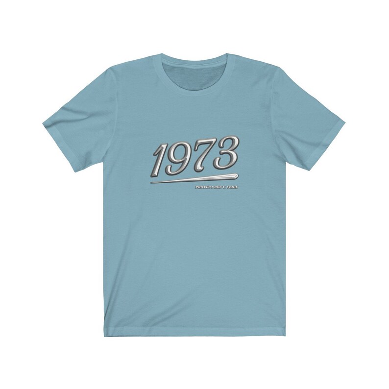 May include: Light blue t-shirt with a silver graphic of the year 1973 and the text "Positive vibes only".