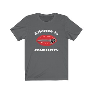 Puede incluir: Una camiseta gris oscuro con el texto "Silence is Complicity" en blanco. Debajo del texto se muestra una boca roja con una cremallera subida.