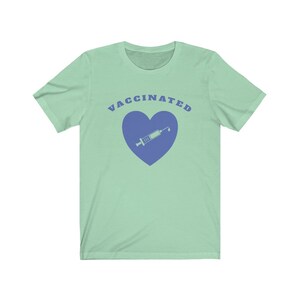 May include: A light green t-shirt with the text "VACCINATED" in blue letters. A blue heart with a syringe inside is below the text.