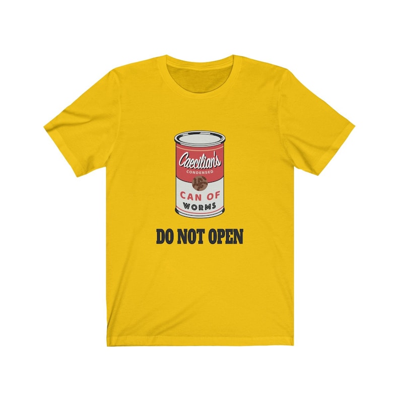 Puede incluir: Camiseta amarilla con un gr&aacute;fico de una lata roja etiquetada "Caecilians Condensed Can of Worms" con el texto "Do Not Open" en negro.