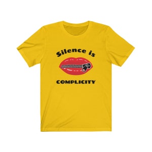 Puede incluir: Camiseta amarilla con un gr&aacute;fico negro de una boca roja con una cremallera subida. El texto "Silence is Complicity" est&aacute; impreso debajo del gr&aacute;fico.