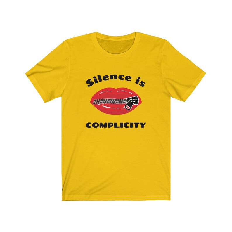 Puede incluir: Camiseta amarilla con un gr&aacute;fico negro de una boca roja con una cremallera subida. El texto "Silence is Complicity" est&aacute; impreso debajo del gr&aacute;fico.