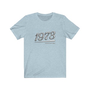 May include: Light blue t-shirt with a silver graphic of the year 1973 with a silver line underneath. The text "IMPORTANT THINGS WERE SIMPLE" is below the year.