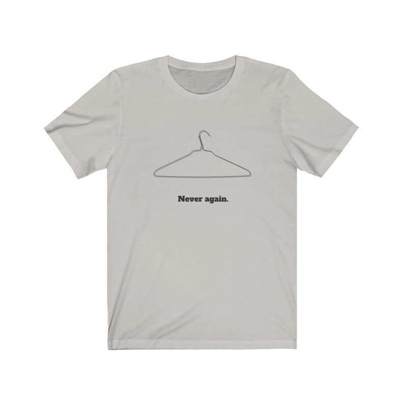 May include: A light gray t-shirt with a black wire hanger graphic and the text "Never again."