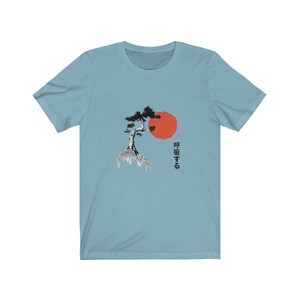 Puede incluir: Una camiseta azul claro con una ilustraci&oacute;n en blanco y negro de un &aacute;rbol en una roca con un sol rojo detr&aacute;s. El texto japon&eacute;s "呼吸する" est&aacute; impreso en el lado derecho de la camiseta.