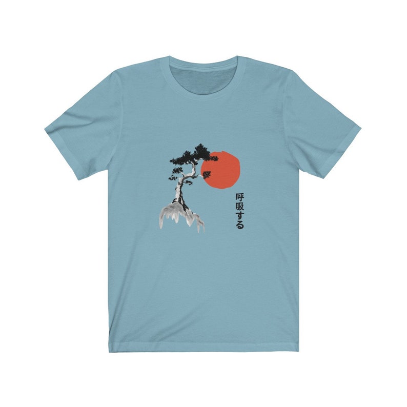 Puede incluir: Una camiseta azul claro con una ilustraci&oacute;n en blanco y negro de un &aacute;rbol en una roca con un sol rojo detr&aacute;s. El texto japon&eacute;s "呼吸する" est&aacute; impreso en el lado derecho de la camiseta.
