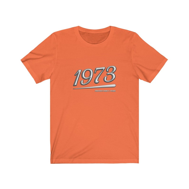 May include: Orange short-sleeved t-shirt with a silver graphic of the year 1973 and the text "PROTECT YOUR WORLD".