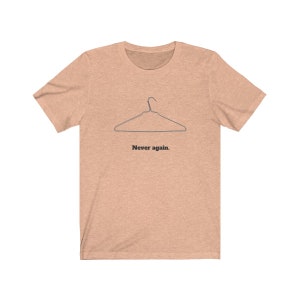 May include: A light peach colored t-shirt with a black wire hanger graphic and the text "Never again." printed below the hanger.