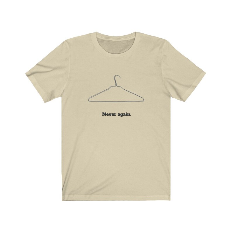 May include: A beige t-shirt with a black wire hanger graphic and the text "Never again."