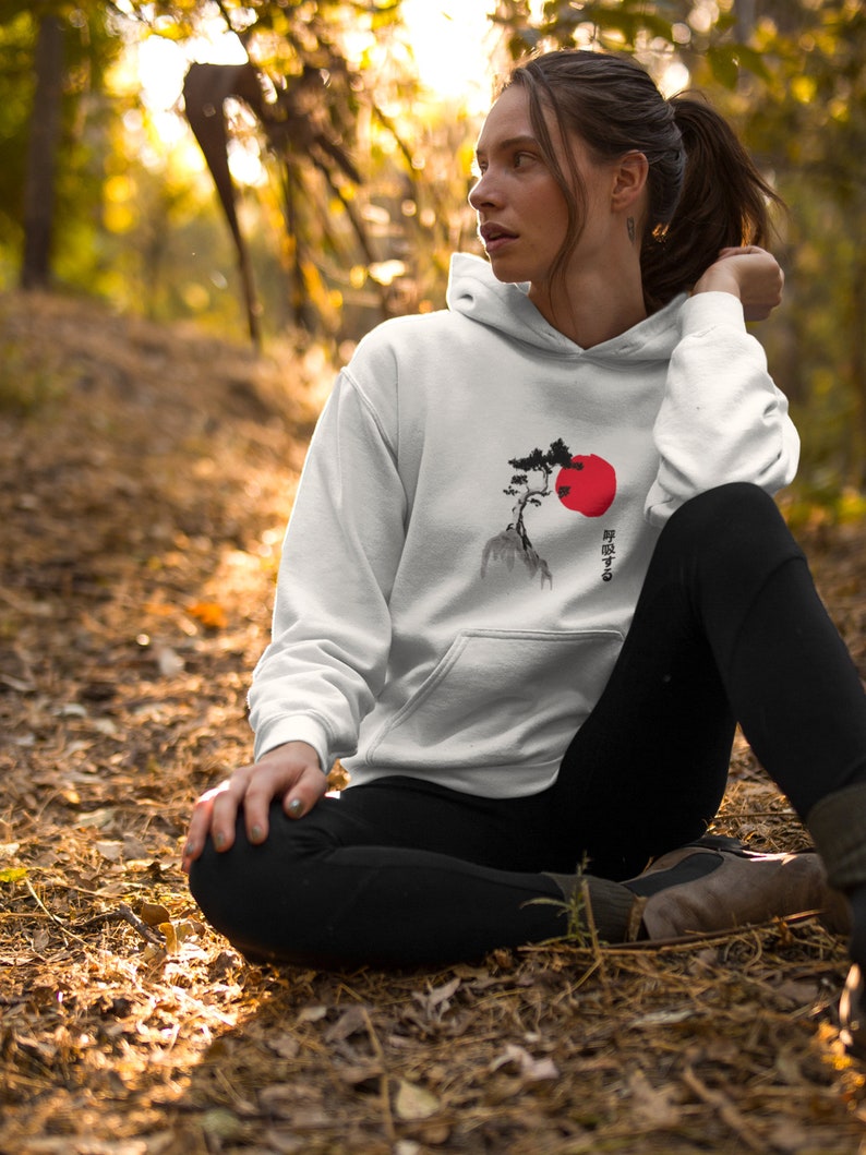 May include: White hoodie with a black and red Japanese-style design of a tree and a rising sun. The text on the hoodie reads "昇る太陽".