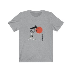 Puede incluir: Una camiseta gris jaspeada con una ilustraci&oacute;n en blanco y negro de un &aacute;rbol y un sol rojo. El texto japon&eacute;s en la camiseta dice "呼吸する".