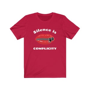 Puede incluir: Camiseta roja con un gr&aacute;fico blanco de una boca con cremallera y el texto "Silence is Complicity".