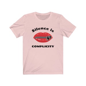 Puede incluir: Camiseta rosa con un gr&aacute;fico negro de una boca roja con una cremallera subida. El texto "Silence is Complicity" est&aacute; impreso debajo del gr&aacute;fico.