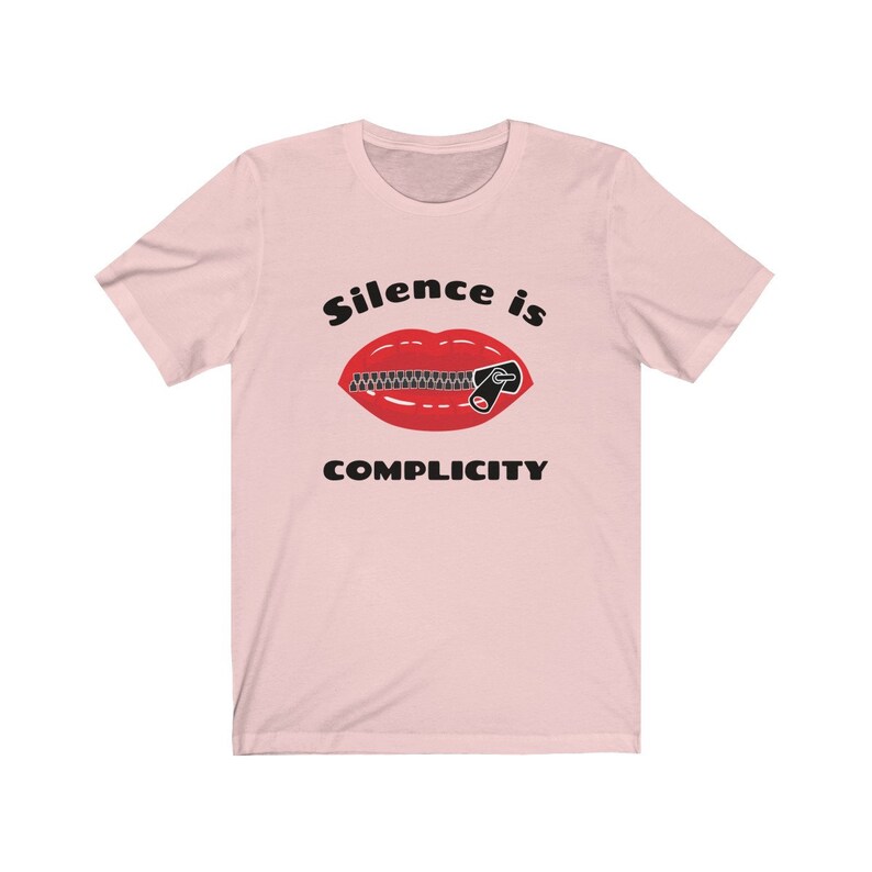 Puede incluir: Camiseta rosa con un gr&aacute;fico negro de una boca roja con una cremallera subida. El texto "Silence is Complicity" est&aacute; impreso debajo del gr&aacute;fico.
