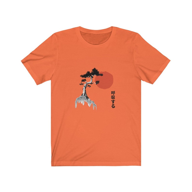 Puede incluir: Camiseta naranja de manga corta con una ilustraci&oacute;n en blanco y negro de un &aacute;rbol en una roca con un sol rojo detr&aacute;s. El texto japon&eacute;s "呼吸する" est&aacute; impreso en el lado derecho de la camiseta.