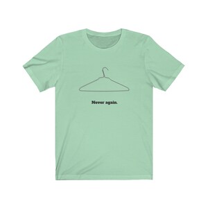 May include: A light green t-shirt with a black wire hanger and the text "Never again." printed on the front.