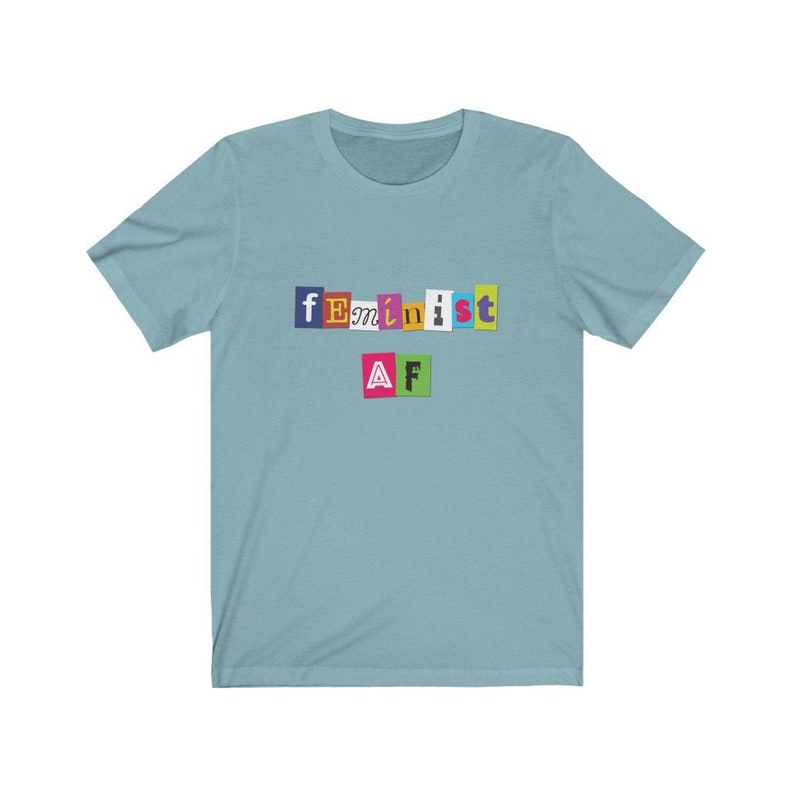 May include: A light blue t-shirt with the text "feminist AF" in colorful, cut-out letters.