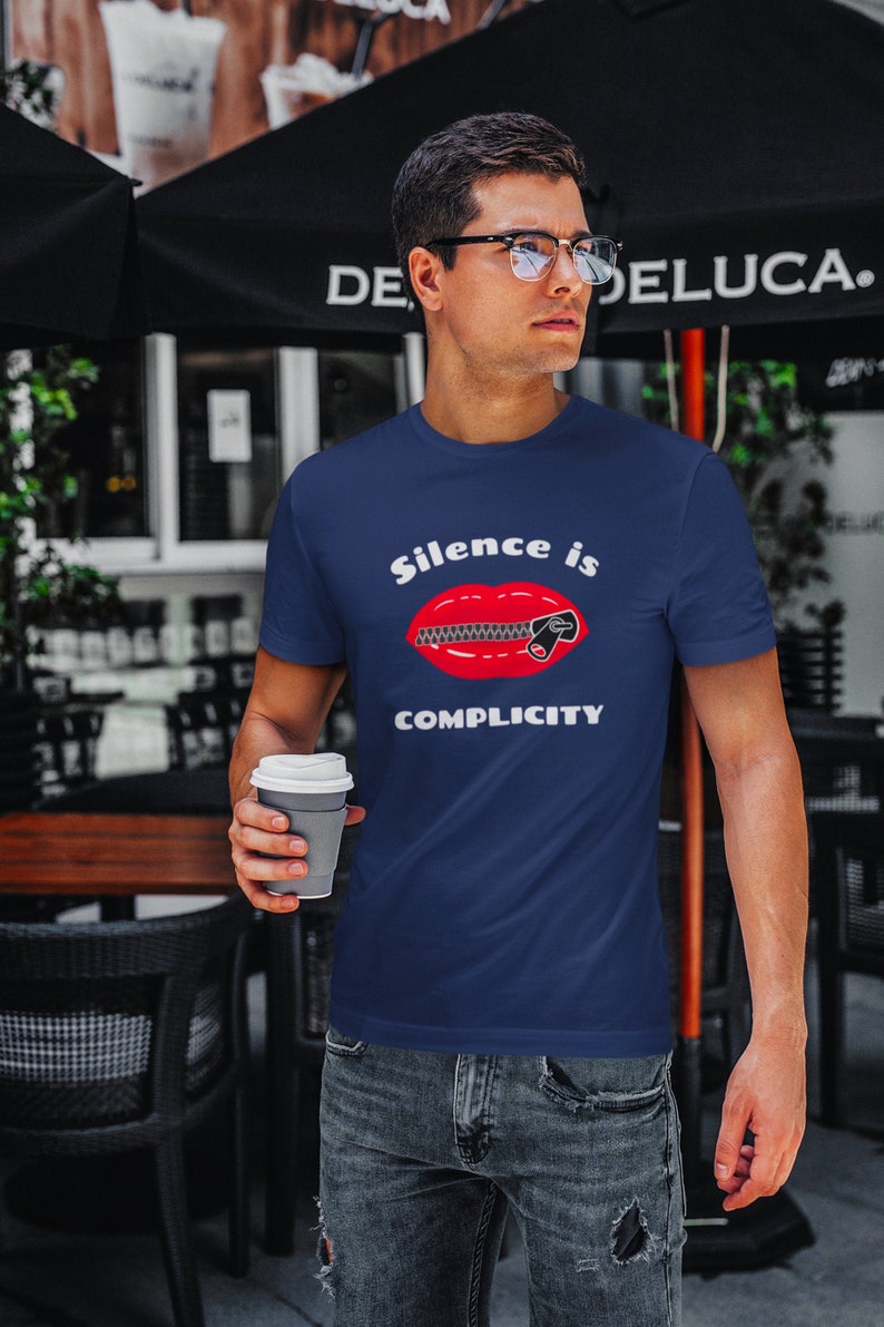 Puede incluir: Una camiseta azul marino con un gr&aacute;fico de boca roja y el texto "Silence is Complicity".