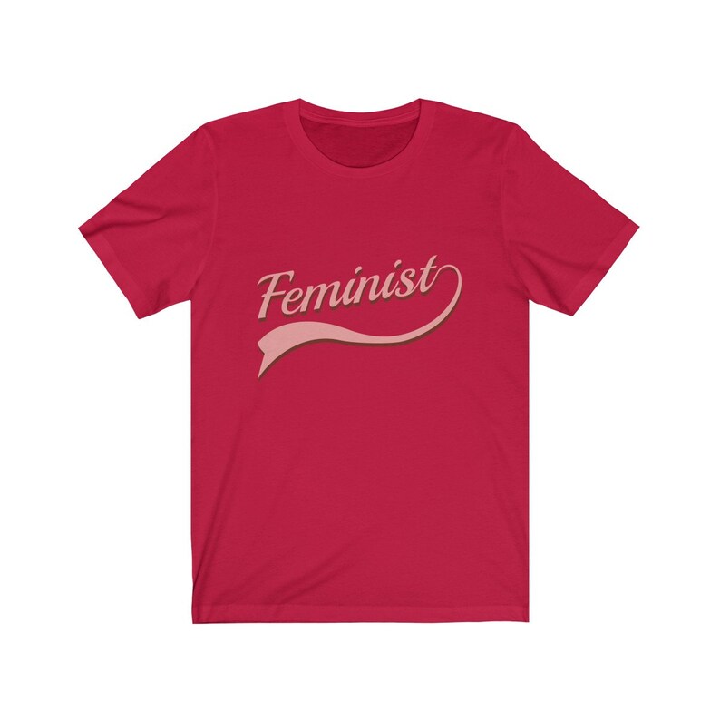 Puede incluir: Camiseta roja con la palabra "Feminista" en letra rosa con una cinta rosa debajo.