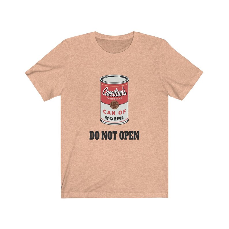 Puede incluir: Una camiseta de color melocot&oacute;n claro con un gr&aacute;fico de una lata roja etiquetada "Caecilians Condensed Can of Worms" con el texto "DO NOT OPEN" debajo de la lata.