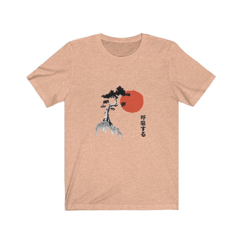 Puede incluir: Una camiseta de color melocot&oacute;n jaspeado con una ilustraci&oacute;n en blanco y negro de un pino japon&eacute;s y un sol rojo. El texto "呼吸する" est&aacute; impreso en negro debajo de la imagen.