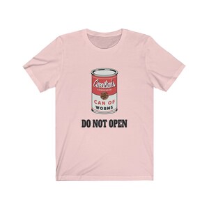 Puede incluir: Camiseta rosa con un gr&aacute;fico de una lata roja etiquetada "Caecilians Condensed Can of Worms" con el texto "Do Not Open" debajo de la lata.