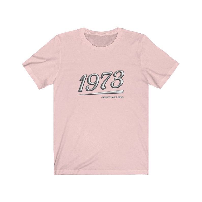 May include: Pink t-shirt with a silver graphic of the year 1973 and the text "Masterfully Crafted Since 1973".