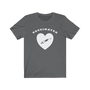 May include: A dark gray t-shirt with the text "VACCINATED" in white letters above a white heart with a syringe inside.