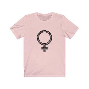 May include: Pink t-shirt with a black and white graphic of the female gender symbol. The graphic has the text "Row, Row, Row your boat gently down the stream" around the symbol.