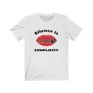 Puede incluir: Camiseta blanca con una boca roja con una cremallera cerrada sobre ella. El texto "Silence is Complicity" est&aacute; impreso debajo de la boca.