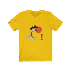 Puede incluir: Camiseta amarilla con una ilustraci&oacute;n en blanco y negro de un &aacute;rbol y un sol rojo. El texto japon&eacute;s "呼吸する" est&aacute; impreso en la camiseta.
