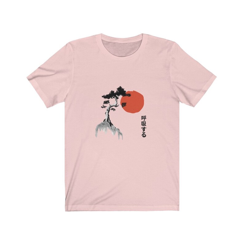 Puede incluir: Camiseta rosa con una ilustraci&oacute;n en blanco y negro de un &aacute;rbol en una monta&ntilde;a con un sol rojo detr&aacute;s. El texto japon&eacute;s "呼吸する" est&aacute; impreso en el lado derecho de la camiseta.